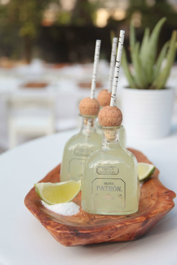 two small bottles are sitting on a wooden tray with limes and salt in them