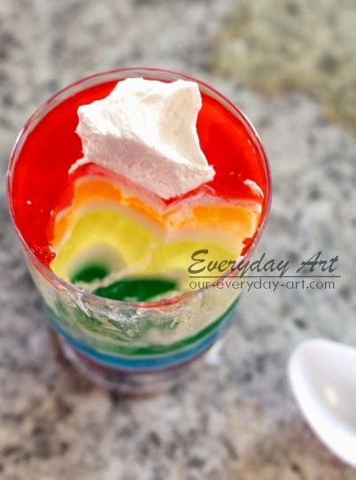 a colorful drink with whipped cream and rainbow colors on the rim, sitting on a marble surface