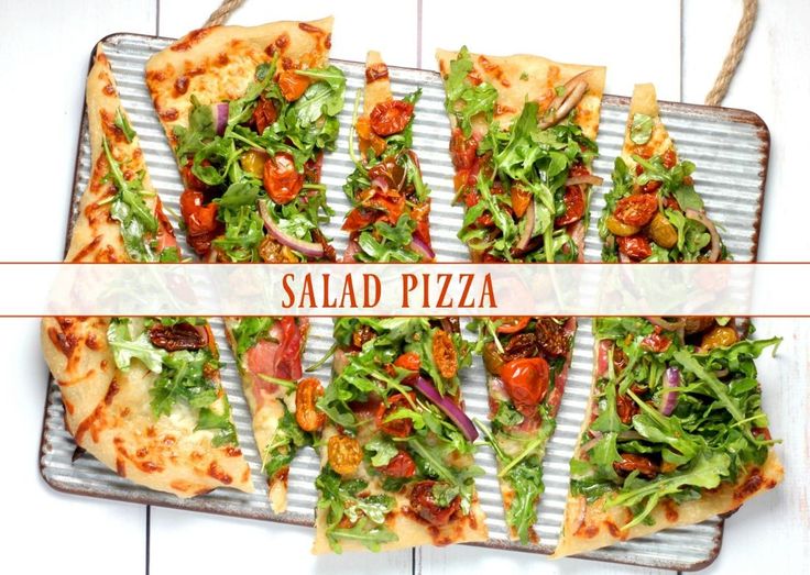 several slices of salad pizza sitting on top of a metal tray next to a white wall