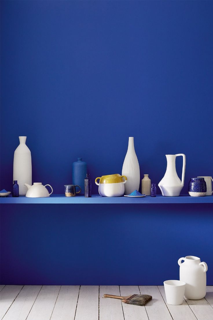 a blue shelf filled with white vases and other items next to each other on a wooden floor