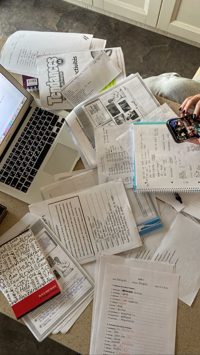 a pile of papers sitting on top of a table next to an open laptop computer