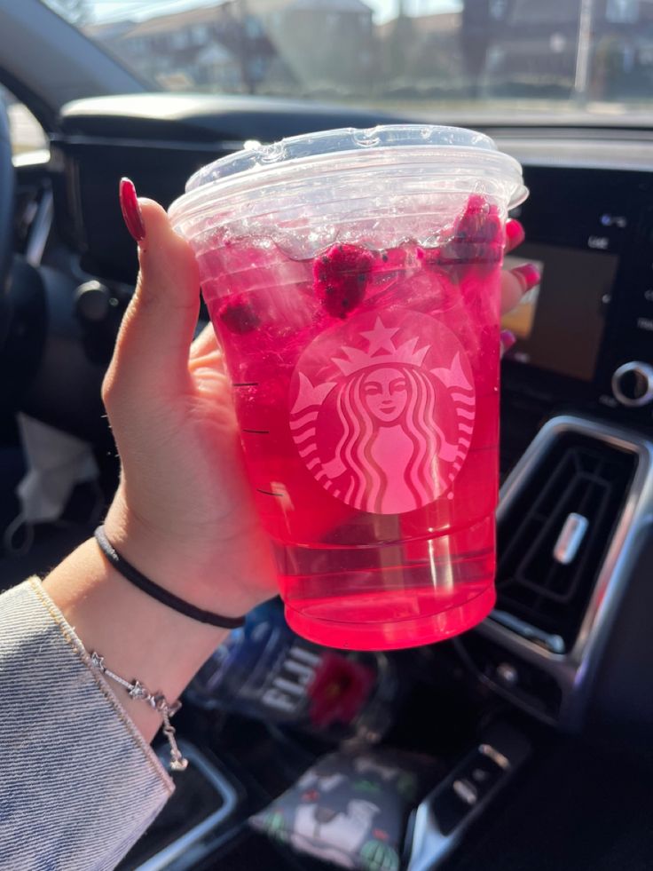 a person is holding up a cup with berries on it in the backseat of a car