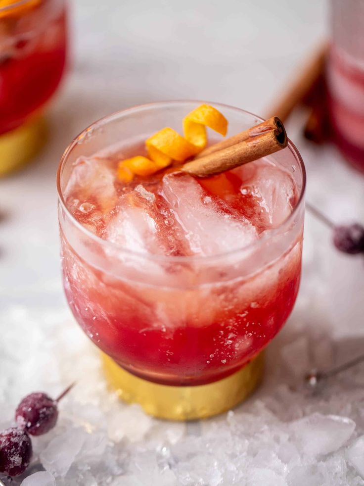 a red drink with an orange garnish on the rim and a cinnamon stick sticking out of it