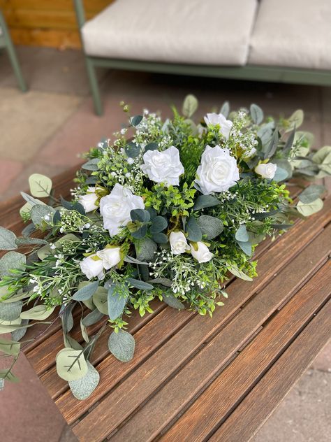 white roses and greenery on a wooden bench