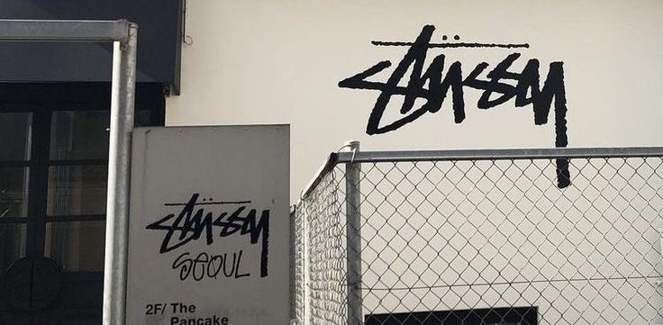 graffiti written on the side of a building near a chain link fence with a door