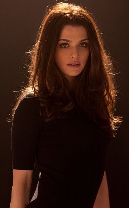 a woman with long hair and black shirt posing in front of a dark background, looking at the camera