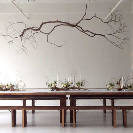 the table is set up with flowers and candles on it, along with branches hanging from the ceiling