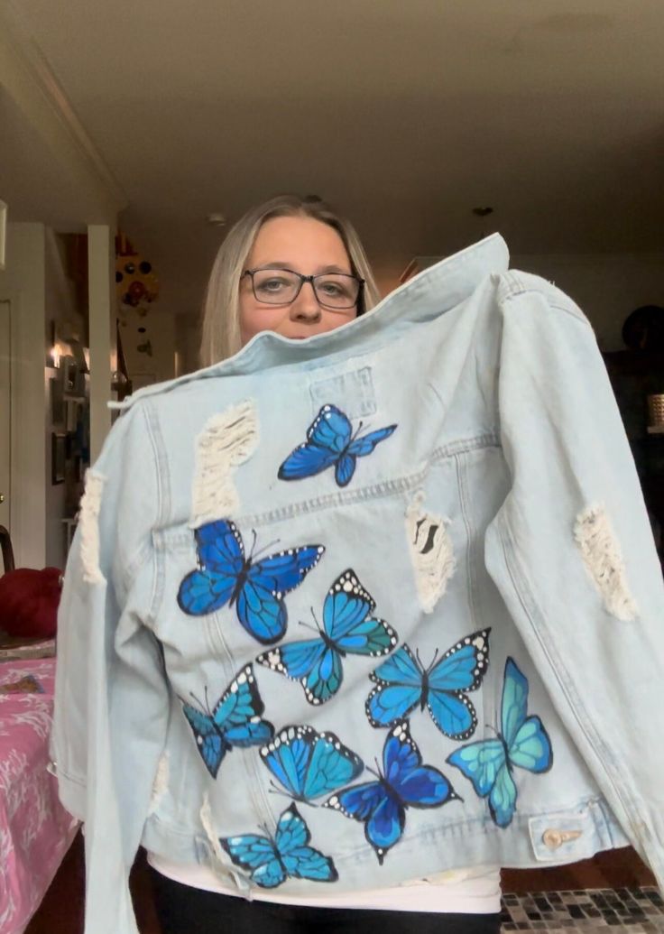 a woman holding up a jean jacket with blue butterflies on it