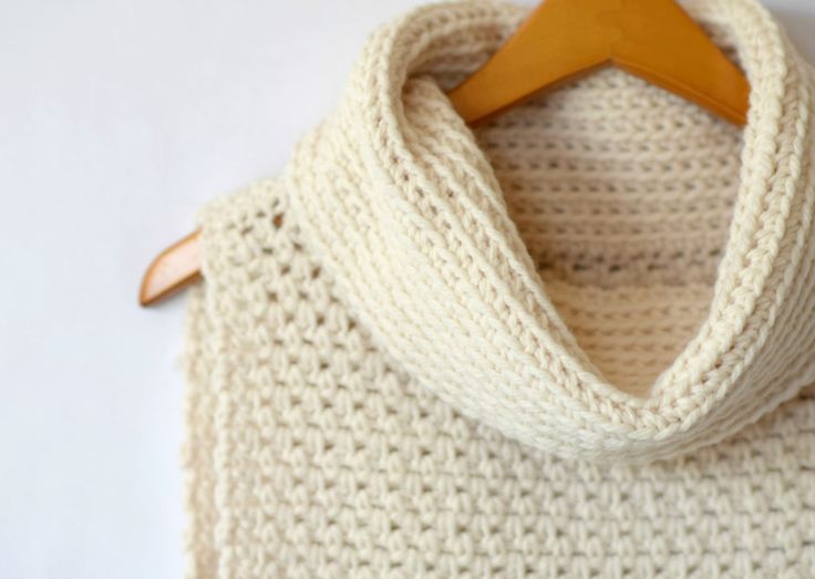 a white knitted sweater hanging on a wooden hanger