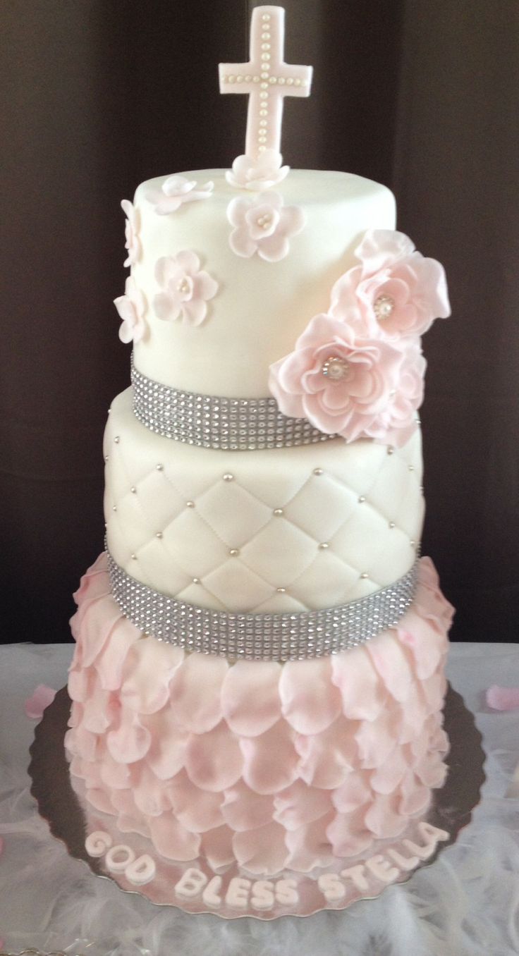 a three tiered cake decorated with pink flowers and a cross on the top layer