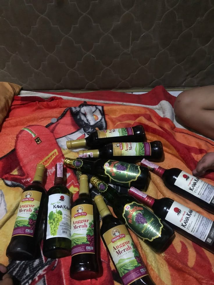 there are many bottles of wine on the bed and one person is laying down next to it