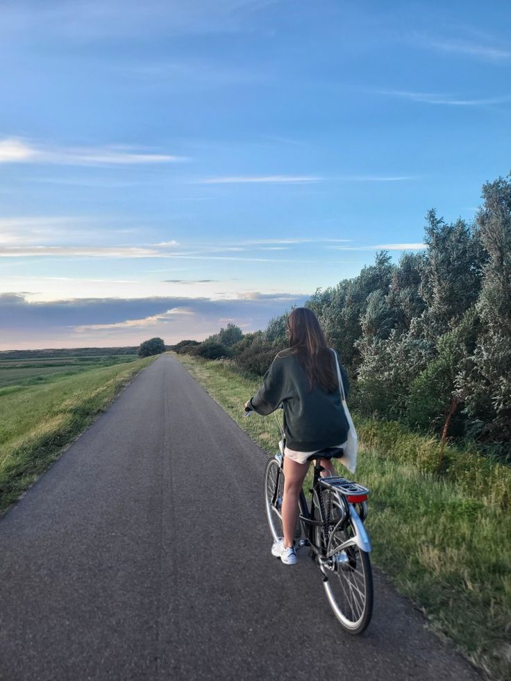 a woman is riding her bike down the middle of an empty road with grass and trees on both sides