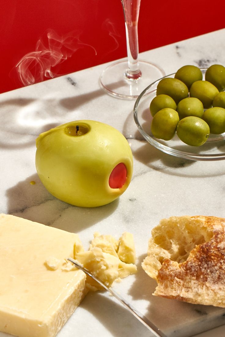 olives, bread and cheese on a table with a glass of wine in the background