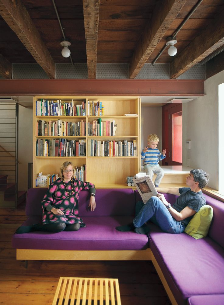 two people sitting on a purple couch in front of a bookshelf with shelves full of books