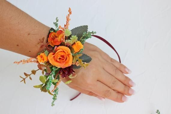 a woman's hand holding an orange wrist corsage with leaves and flowers