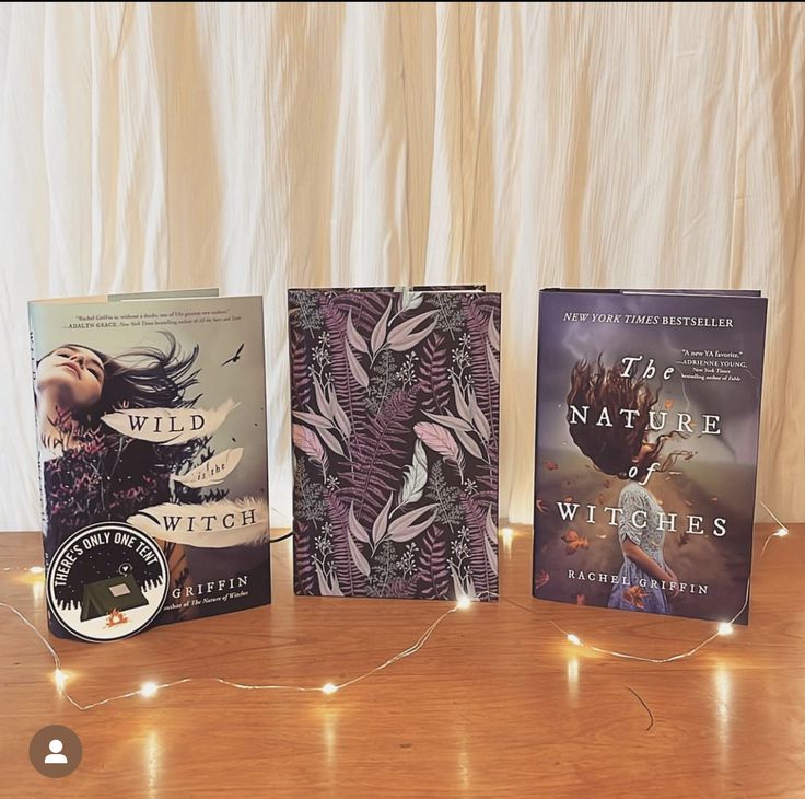 three books sitting on top of a wooden table next to a string of fairy lights