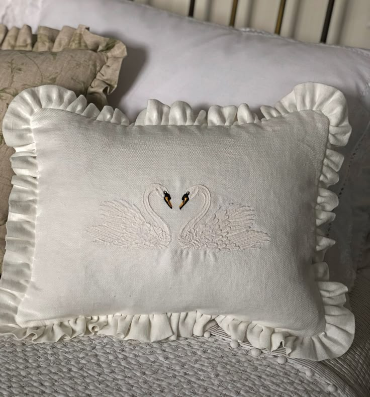 two white pillows on a bed with ruffled edges and one has a black bird embroidered on it