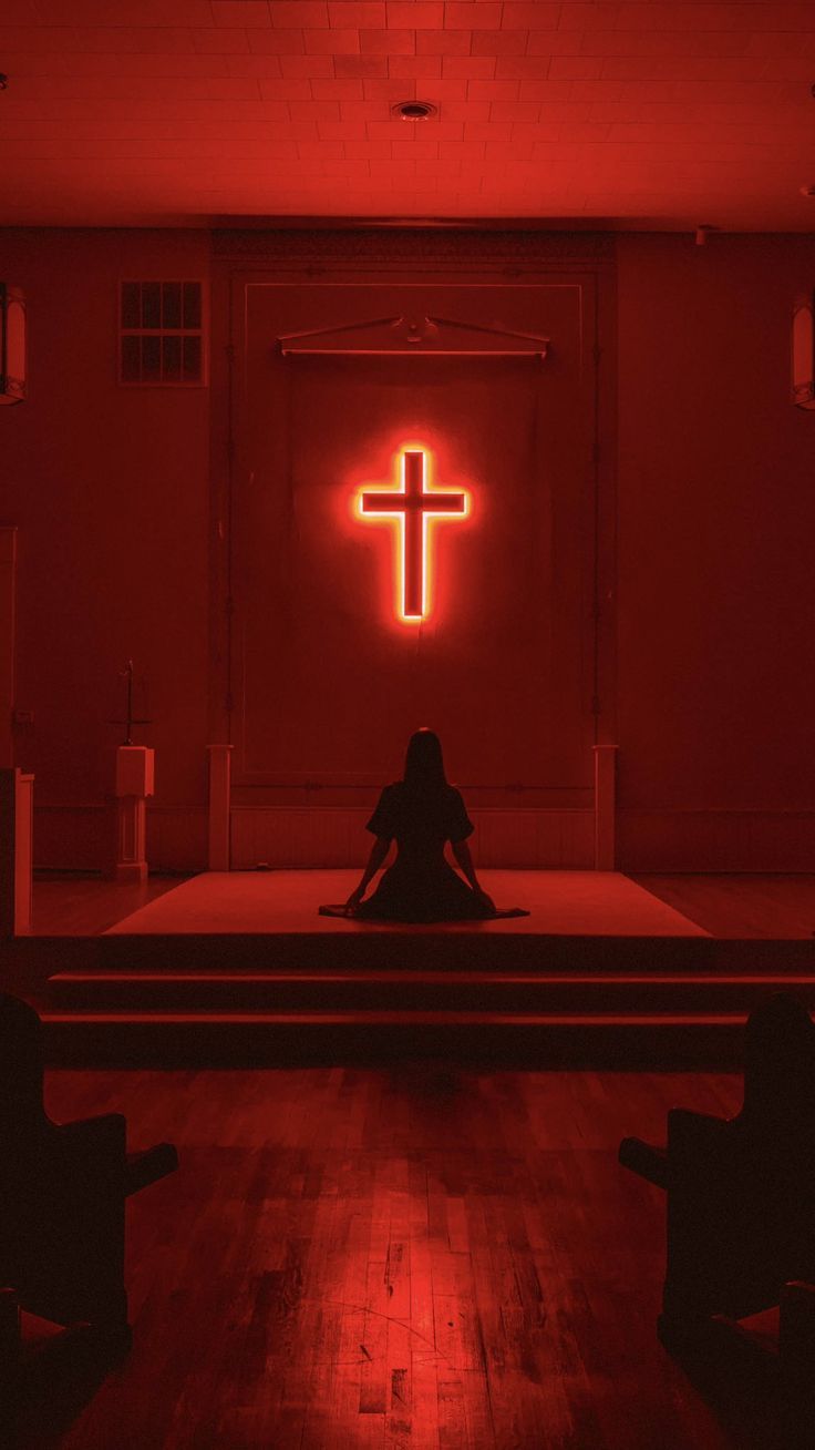 a person sitting on a bench in front of a cross lit by a red light