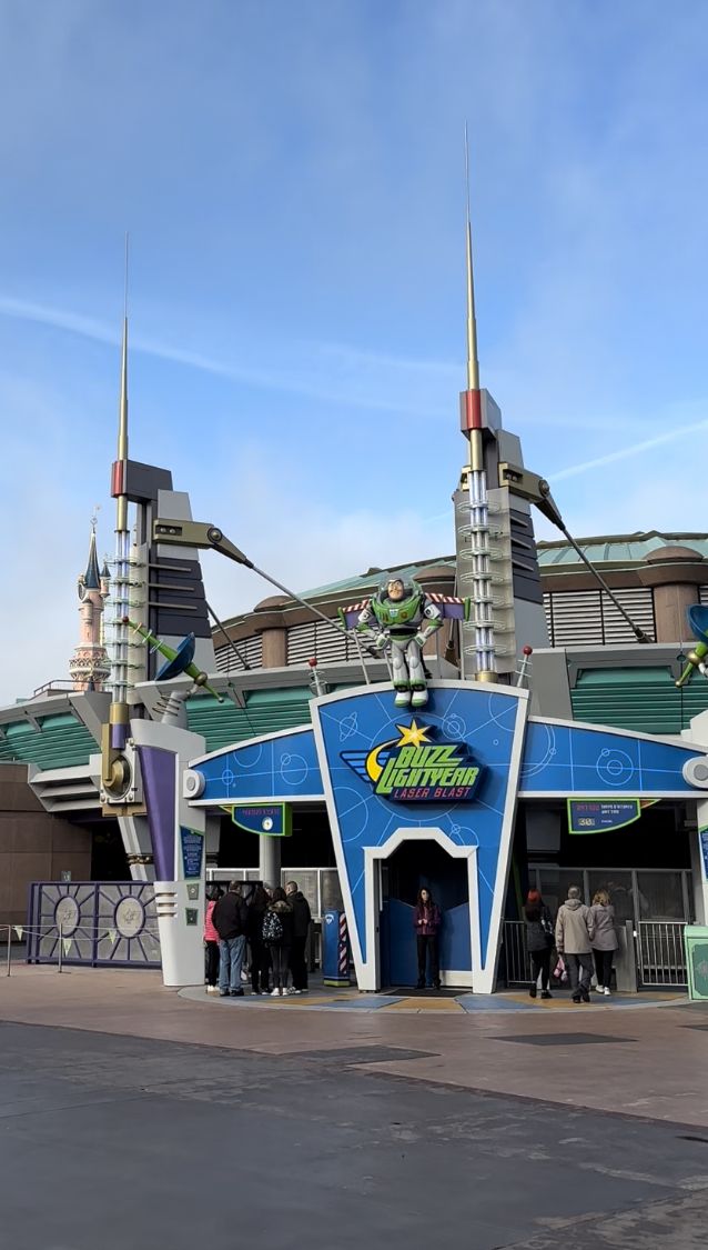 the entrance to an amusement park with people standing in front and looking up at it