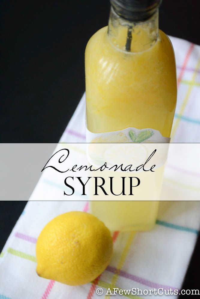 lemonade syrup in a glass bottle next to two lemons on a table cloth