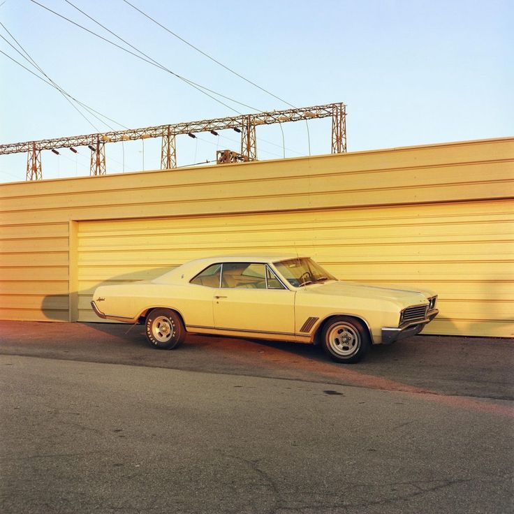 an old car is parked in front of a yellow building with power lines above it