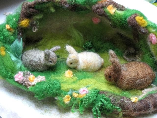 three small stuffed animals are in a miniature garden setting on a white cloth covered napkin