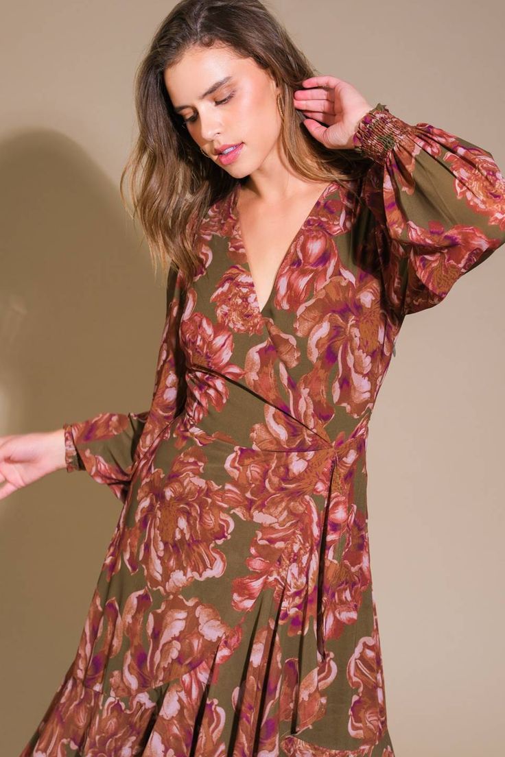 a woman in a floral print dress poses for the camera with her hands on her head