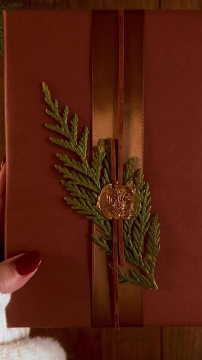 a person holding a red box with a green leaf decoration on it's side