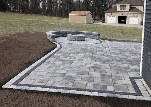 a brick patio in the middle of a yard with a fire pit on one side