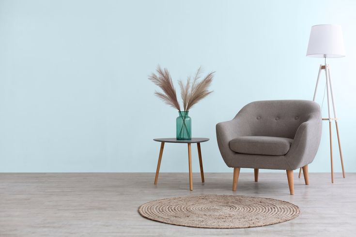 an empty room with a chair, lamp and vase on the floor in front of it