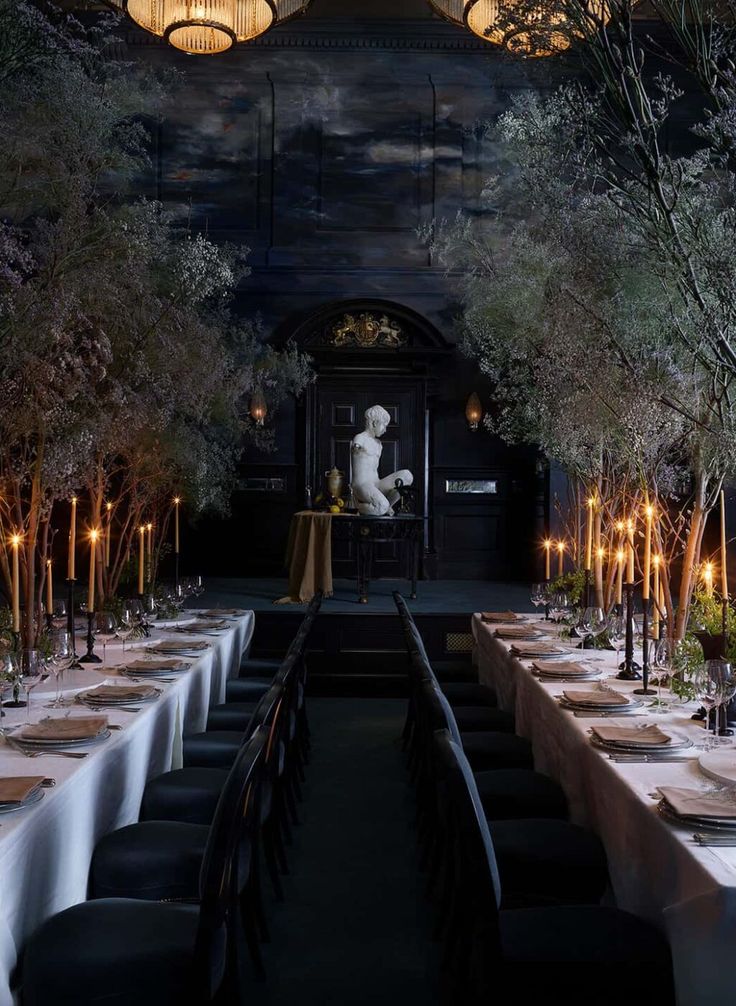 a long table with white linens and candles in front of a large painting on the wall