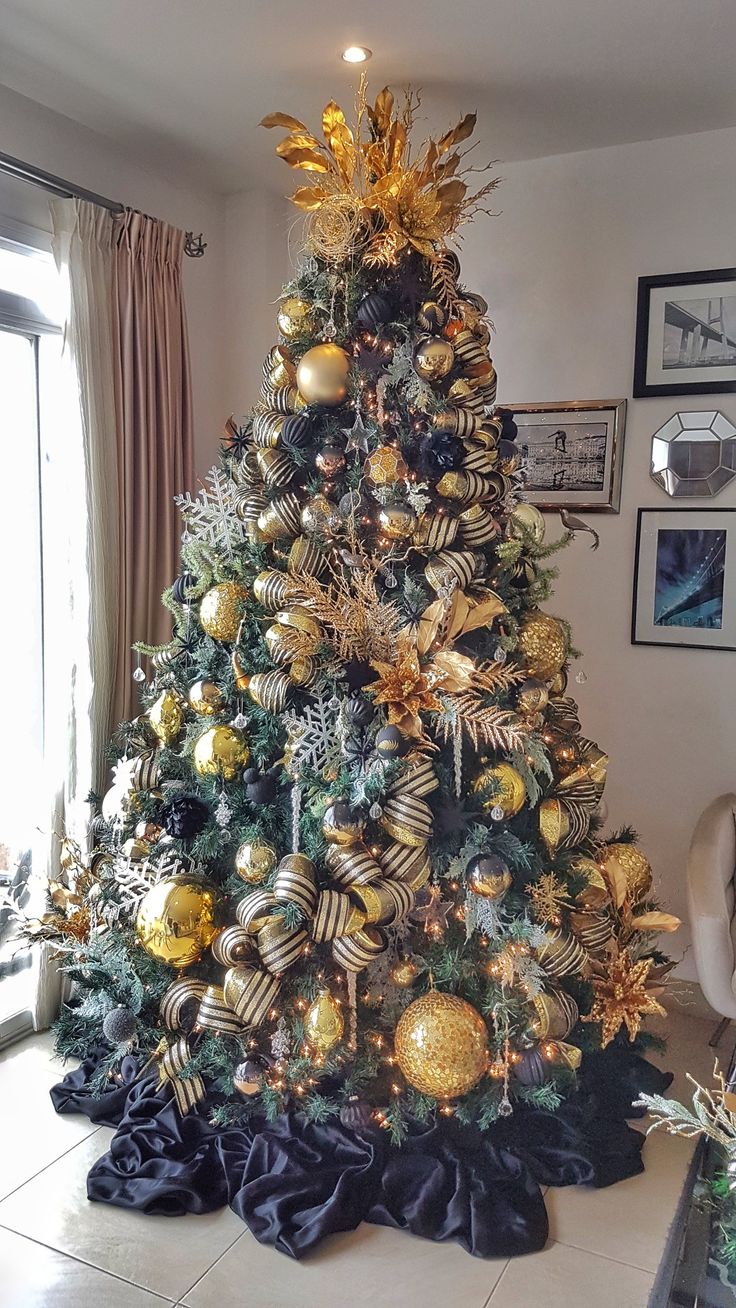 a decorated christmas tree with gold and silver ornaments on it in a living room area