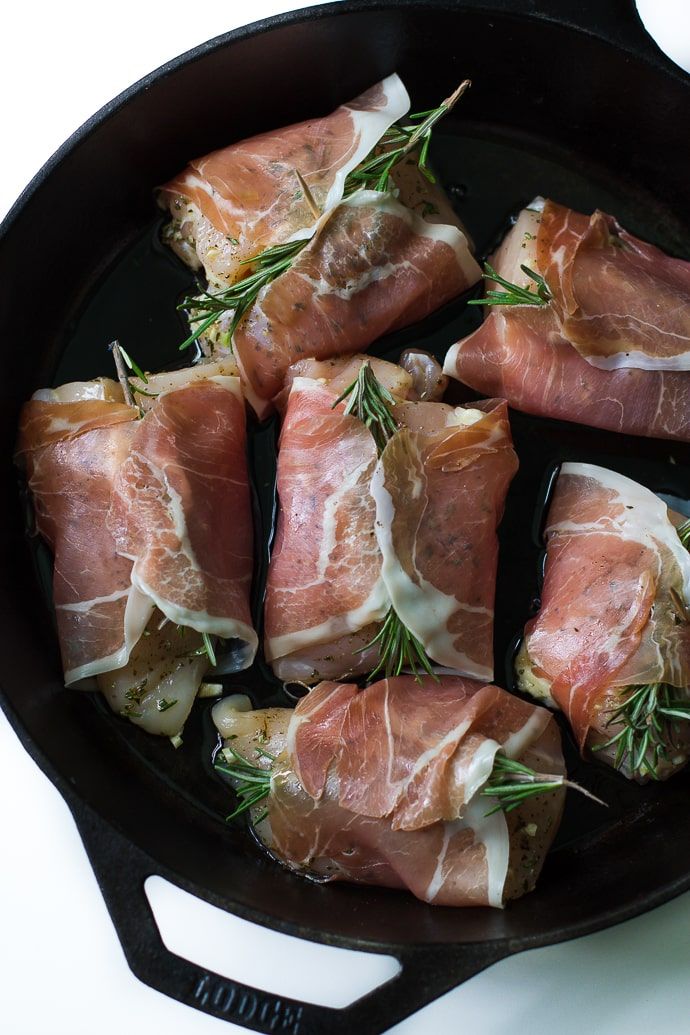 several pieces of meat in a black skillet on a white counter top with rosemary sprigs