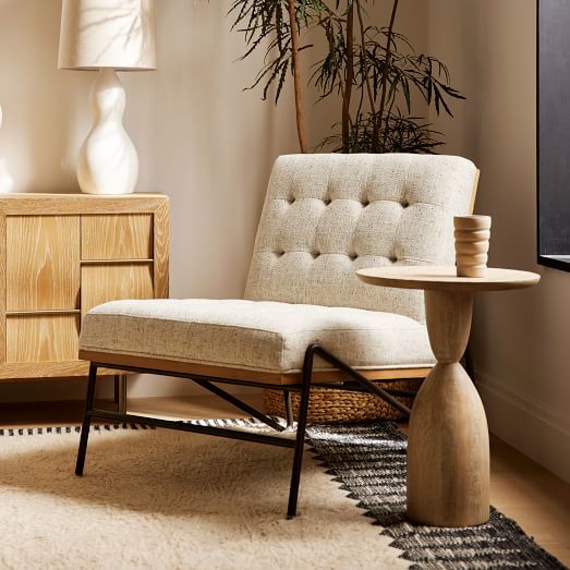 a living room with a chair, table and potted plant on the sideboard