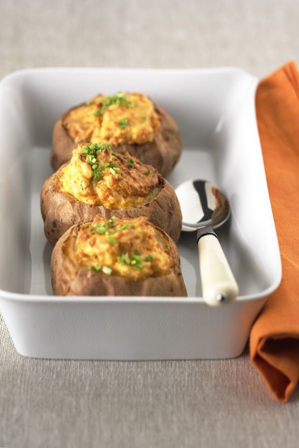 three baked potatoes in a white dish with a spoon on the side and an orange napkin next to it