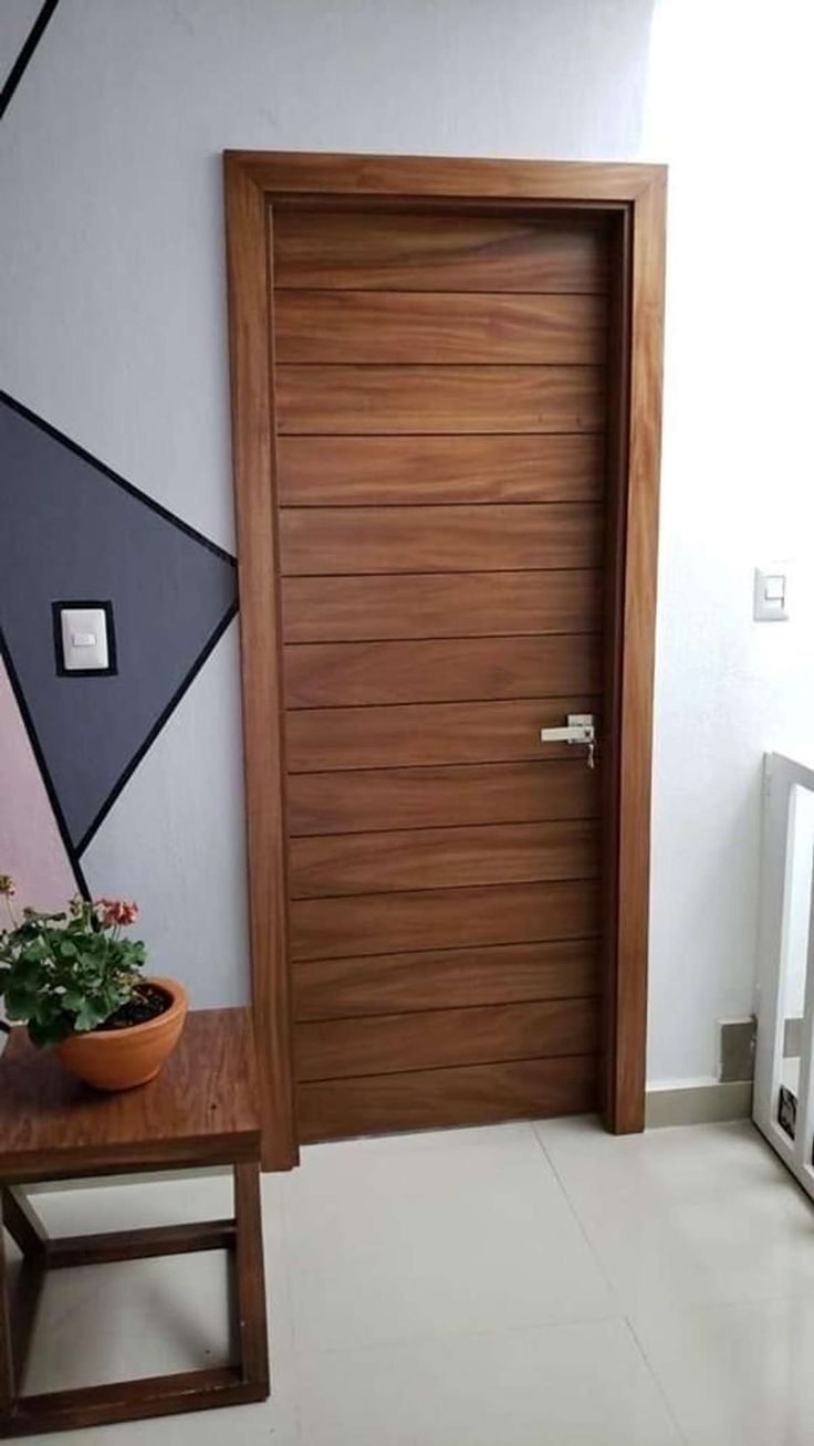 a wooden door in a white room with a potted plant on the side table