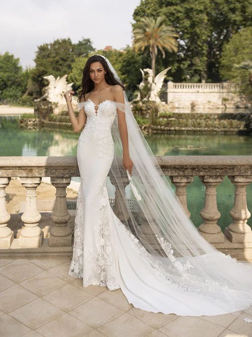 a woman in a wedding dress standing on a balcony with her veil blowing in the wind