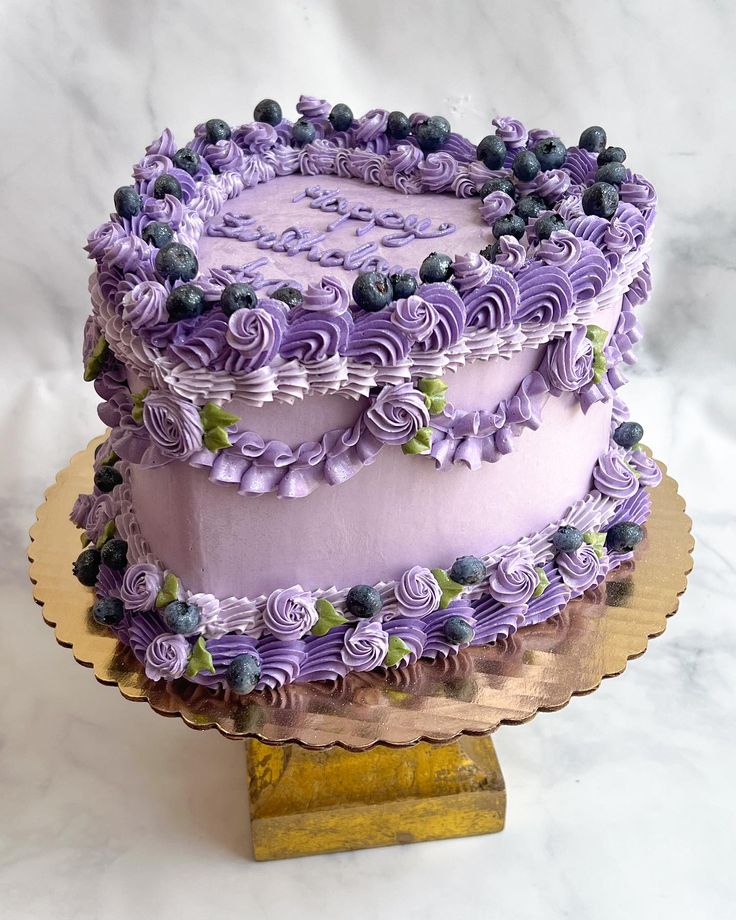 a cake with purple frosting and blueberries on top sitting on a gold plate