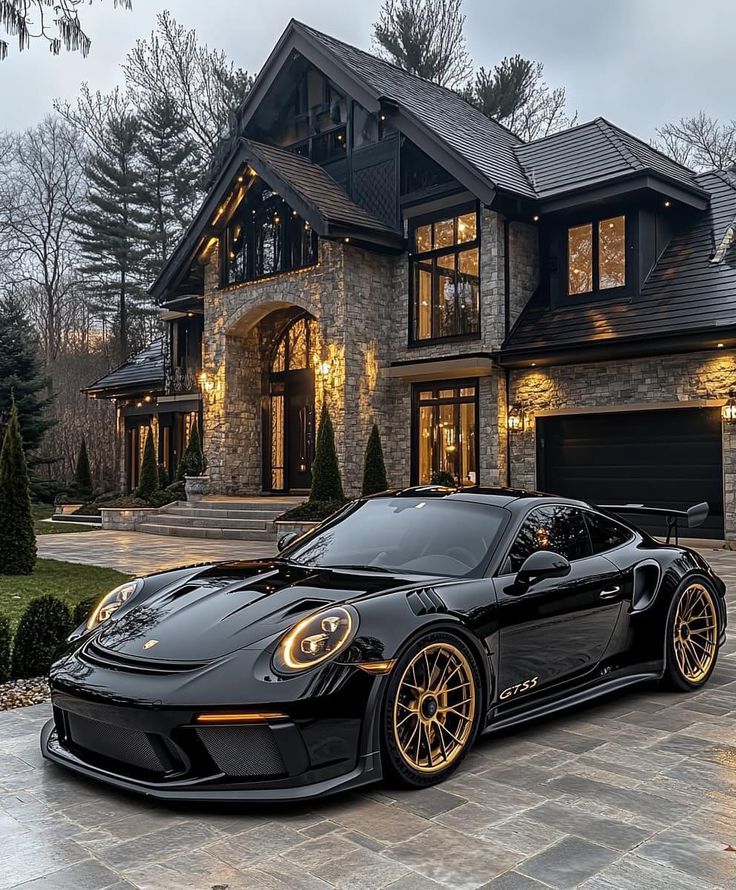 a black sports car parked in front of a large house with lights on the windows