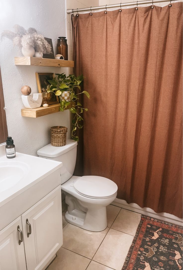 a white toilet sitting next to a bathroom sink under a shower curtain with a plant on top of it