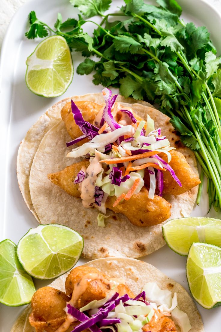 two fish tacos with cole slaw and lime wedges on a white plate