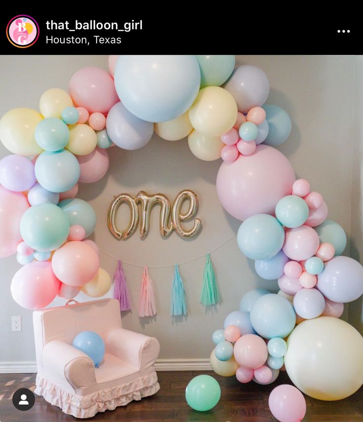 a balloon arch with balloons, tassels and one sign on the wall above it