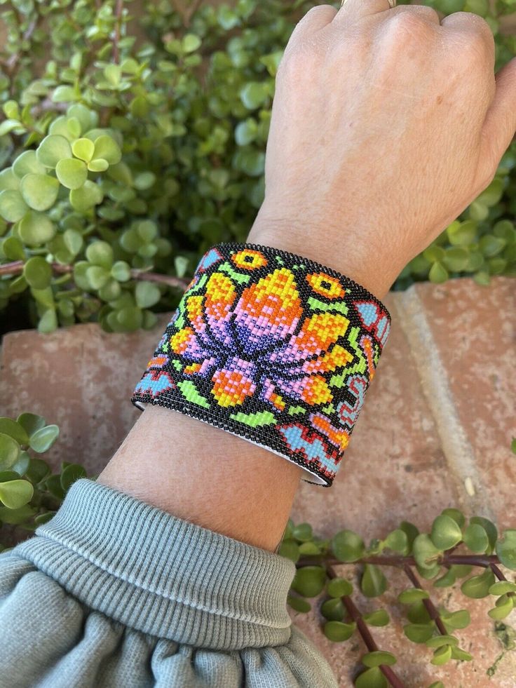 a person wearing a bracelet with beads on it's wrist and green plants in the background