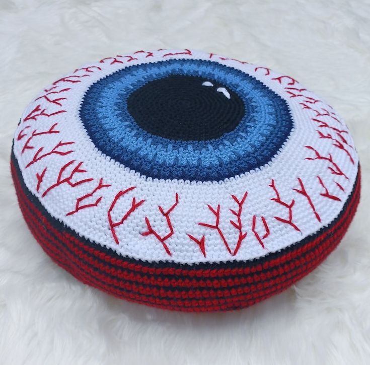 a crocheted cushion with an eyeball design on the bottom and red, white, and blue stitches