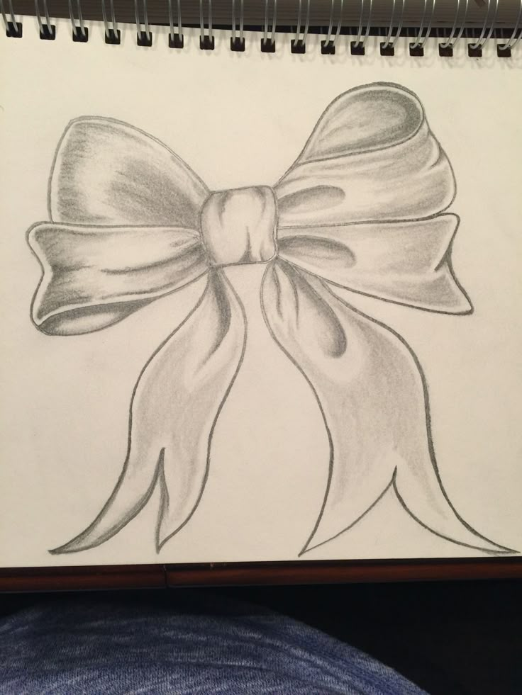 a pencil drawing of a bow on top of a sheet of paper with someone's feet in the background