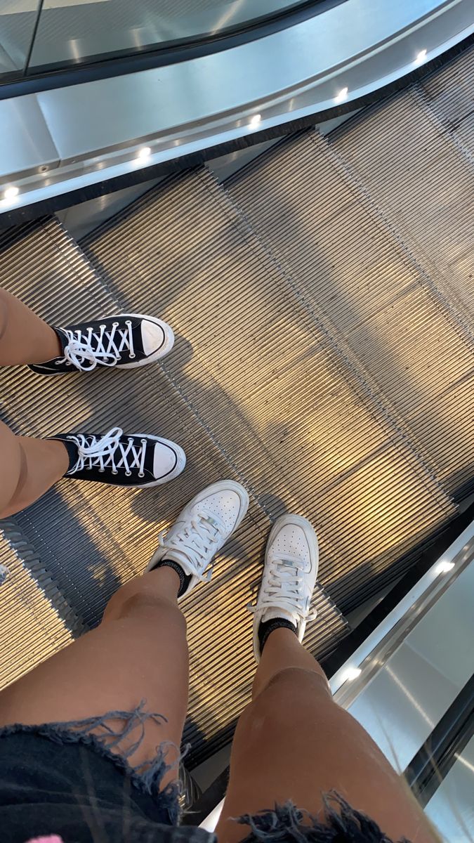 two people standing on an escalator with their feet up and one is wearing white sneakers