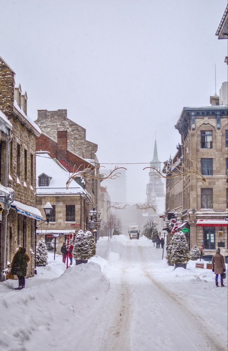 a snowy street with people walking down it and buildings in the background on a cloudy day