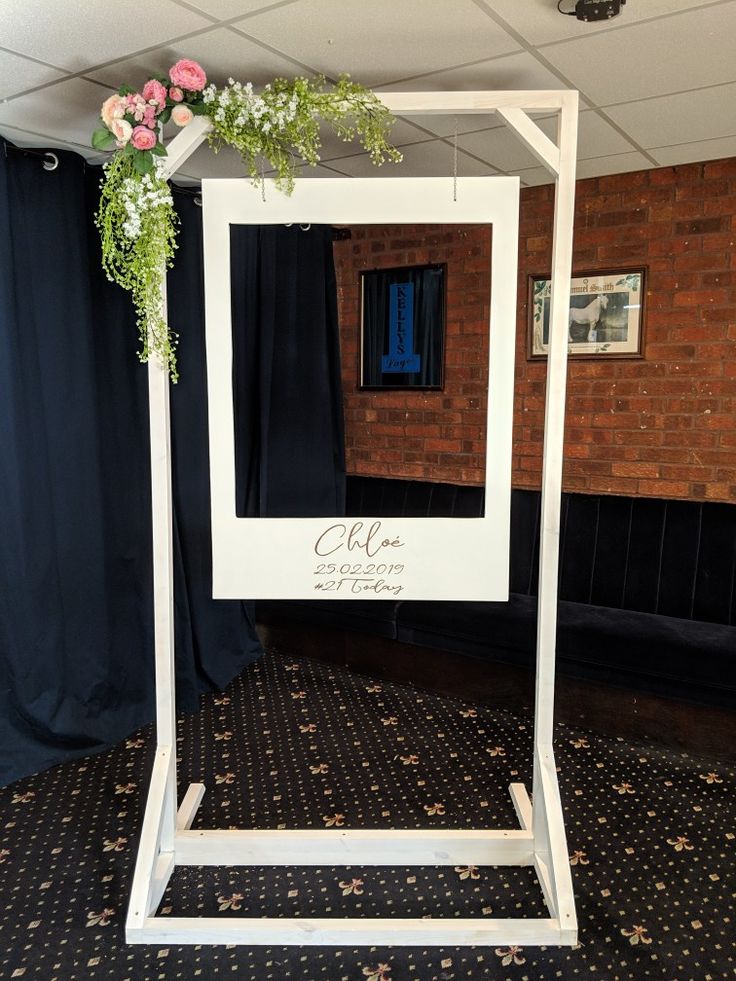 a white frame with flowers on it in front of a brick wall and black curtains