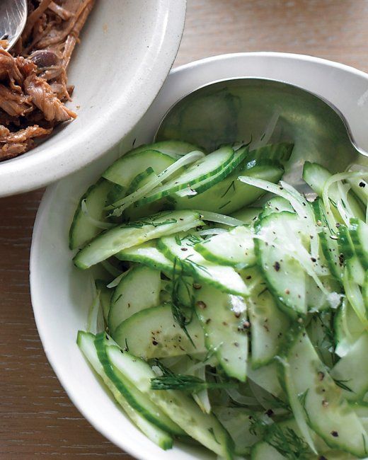 cucumbers and other vegetables are in a bowl next to a spoon on a table