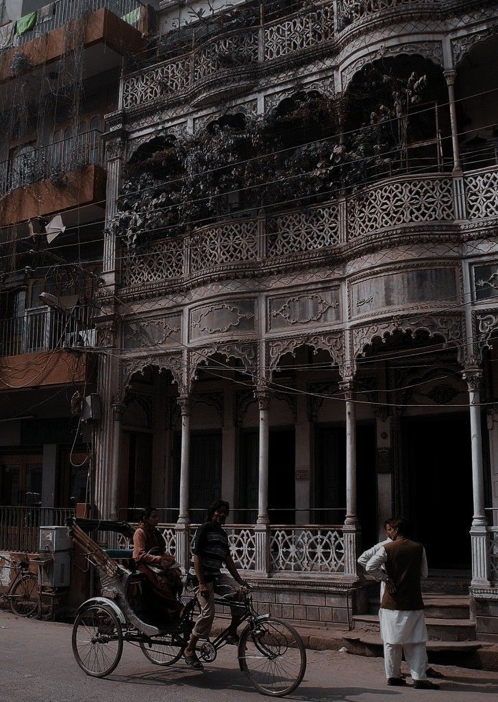 two men are riding on a horse drawn carriage in front of an old, run down building